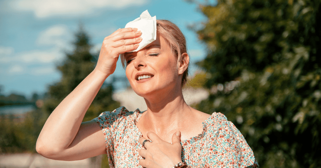 woman experiencing normal hot flashes with tissue on forehead outdoors in nature wearing sundress