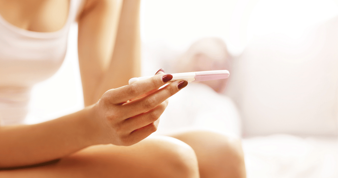 woman holding positive pregnancy test in bed with light background