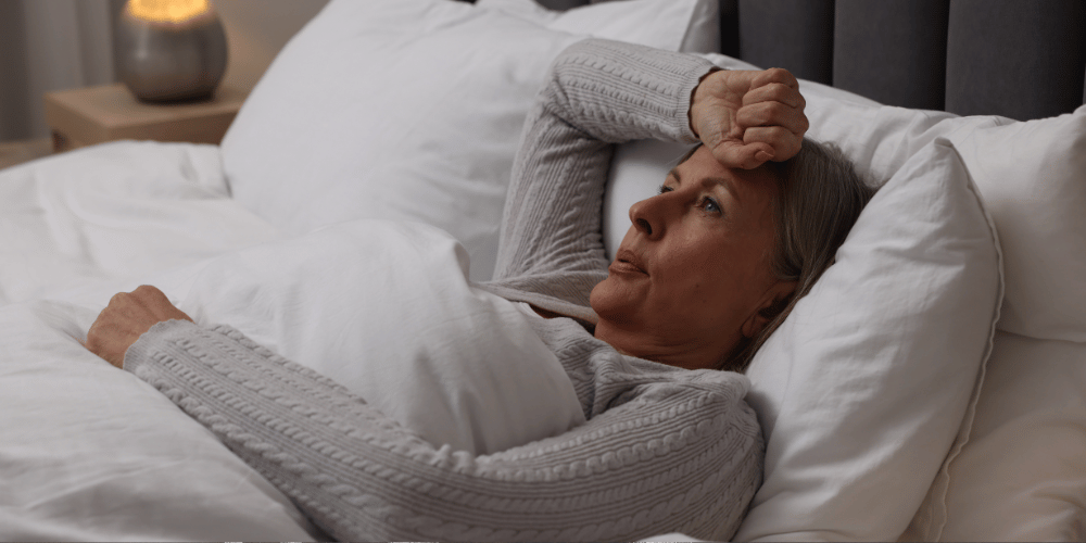 The image captures a person lying in bed, possibly asleep or resting. The person is surrounded by blankets and pillows, suggesting a cozy and comfortable setting. The photo focuses on the human face and the bedding.