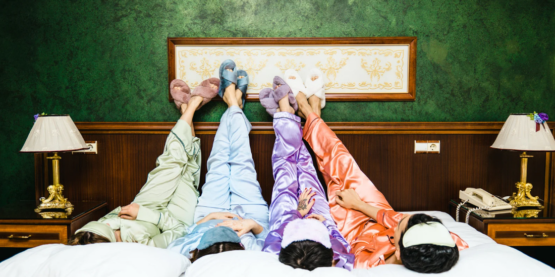 Four people in pajamas relaxing on a bed, shown from the waist down with colorful slippers, a green wall, and decor details.v