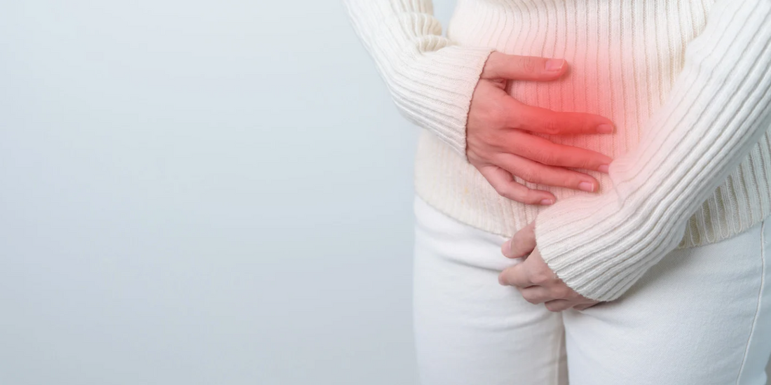 A person in a white sweater is holding their stomach with both hands, indicating discomfort or pain