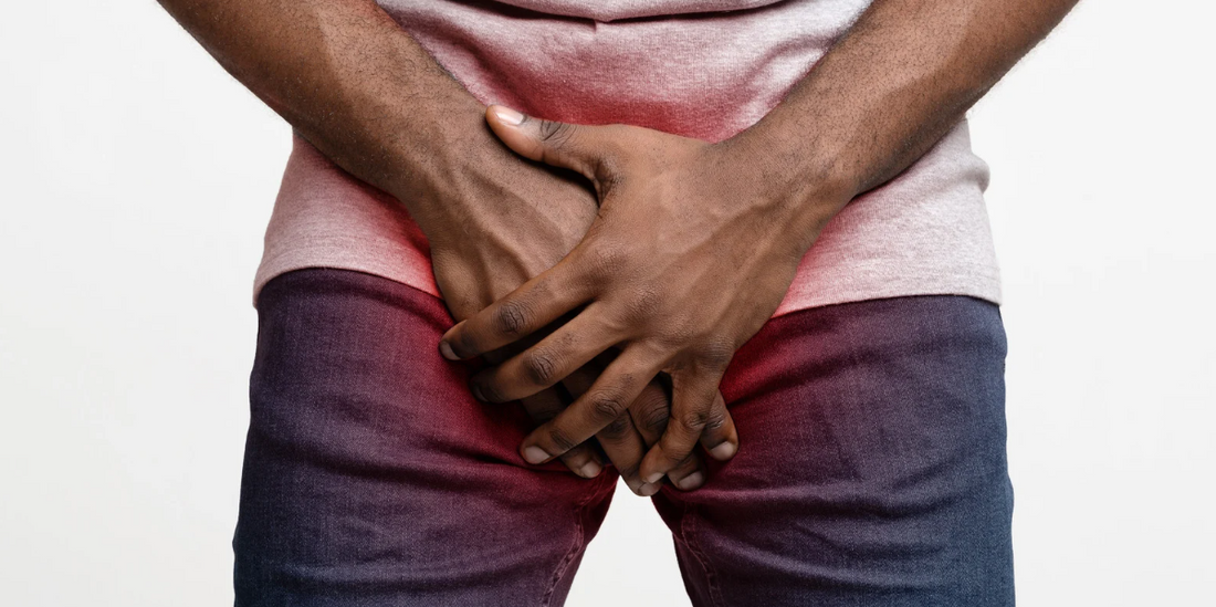 A man is holding his groin area with both hands near the crotch on a white background. 