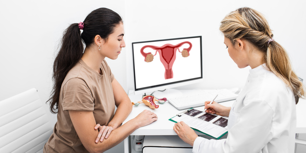 The image shows a woman showing something on a paper to another woman. The setting appears to be indoors, possibly in a healthcare or medical environment. The women are likely discussing something related to their job.