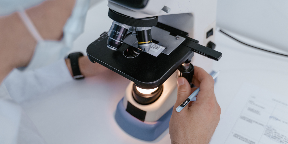 The image shows a person using a microscope. The tag includes microscope, optical instrument, scientific instrument, indoor, and person.