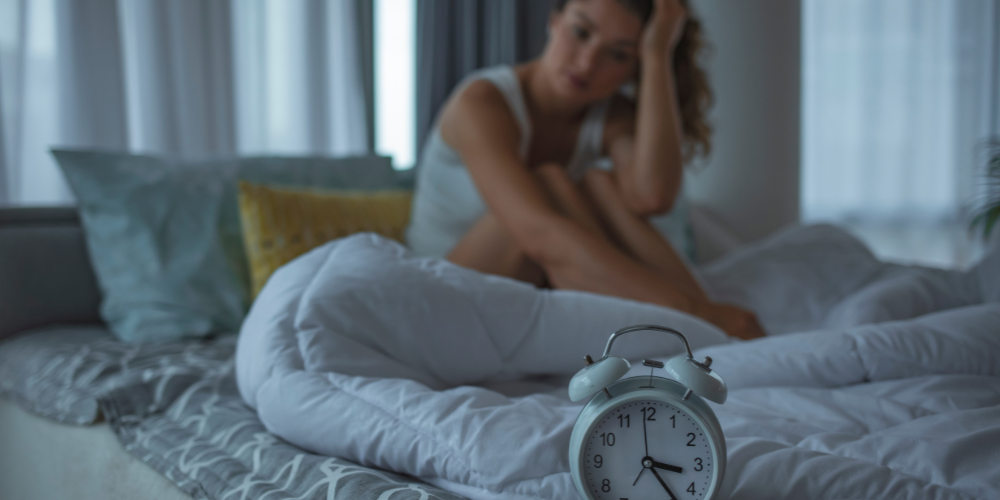 The image shows a woman laying on a bed with a clock on the wall behind her. The clock appears to be showing the time between 10 and 4.