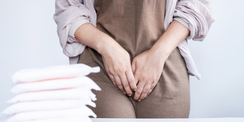 The image shows a woman covering her pelvic area with her hands.