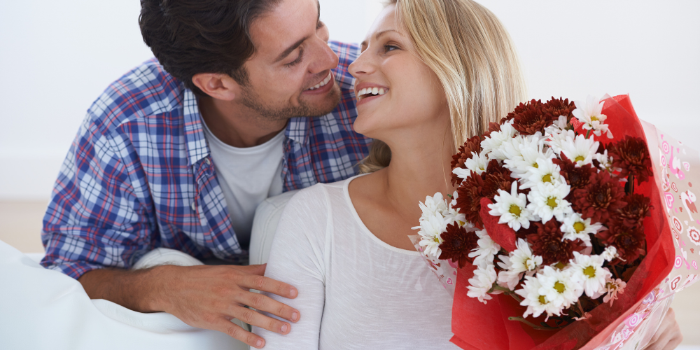 The image shows a man and a woman holding flowers. It is likely a romantic or wedding-related scene.