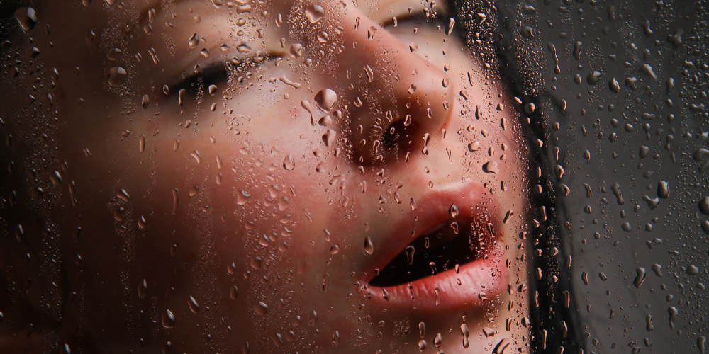 The image shows a person's face being covered in water, possibly from rain. The focus is on the eyelashes and facial features of the person.