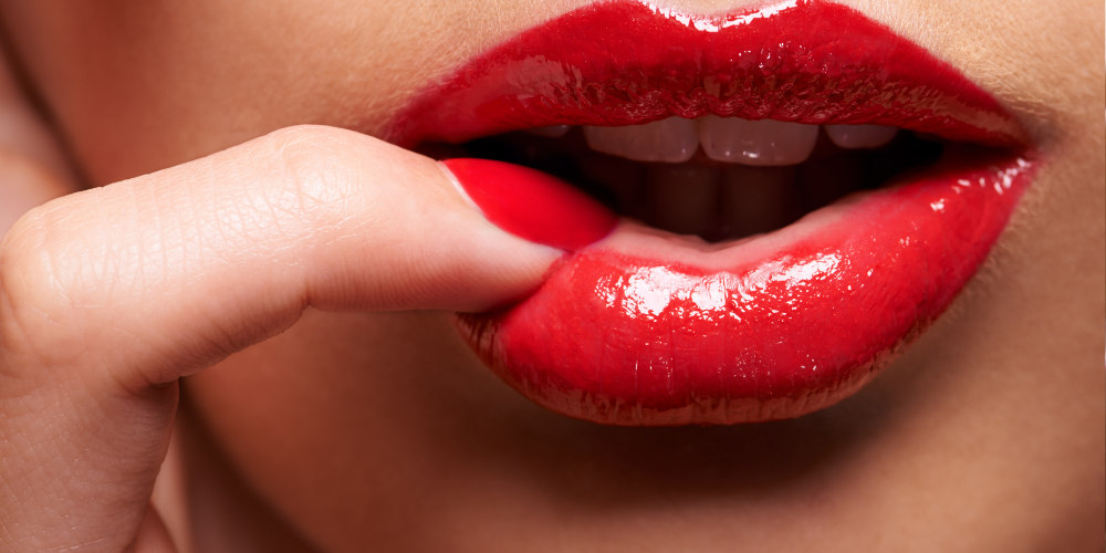 The image is a close-up of a person's open mouth. It features red lipstick and details of the lips, teeth, and tongue.