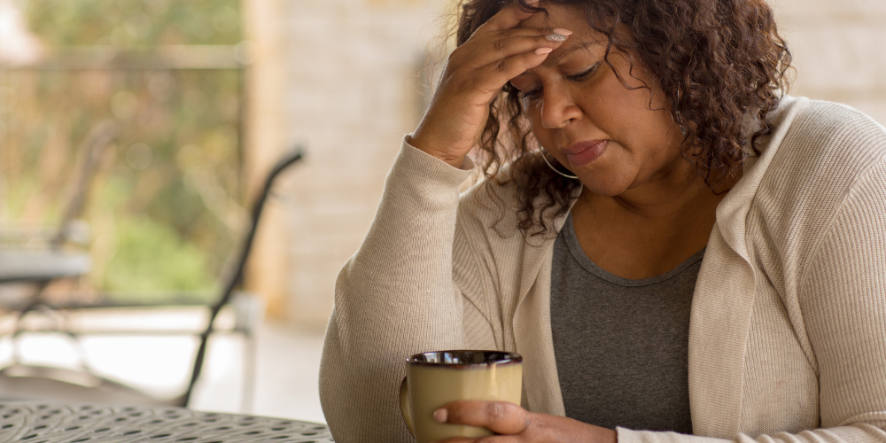 The image shows a woman sitting outdoors while holding a cup of coffee.