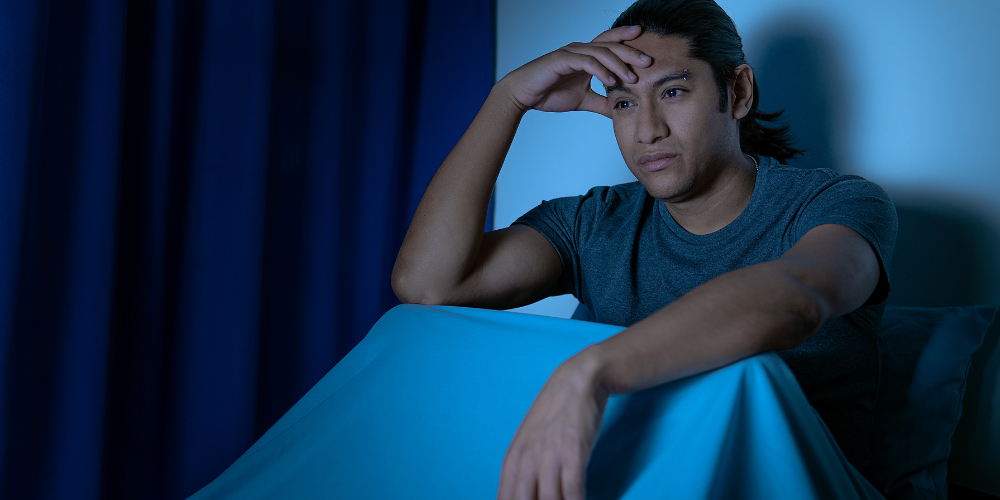 The image features a person with their hand on their head. It is an indoor portrait of a man wearing a blue shirt.