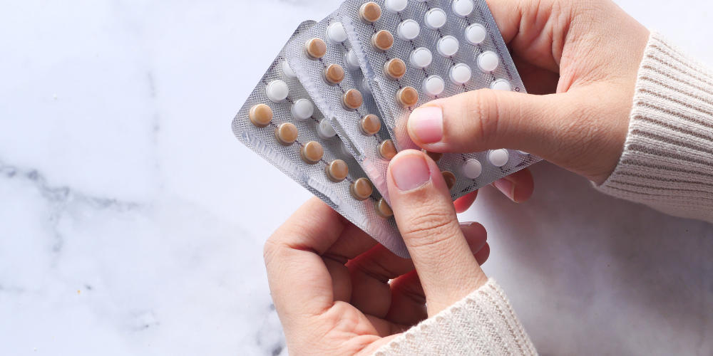 The image shows a person holding a pile of pills. The person's hand is visible, with focus on the fingers and thumb.