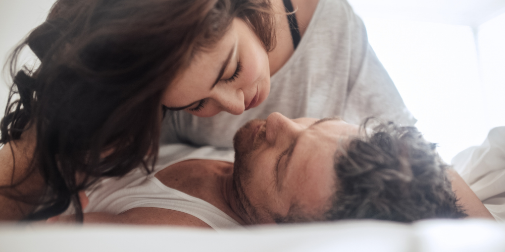 The image shows a woman and a man getting intimate in bed.