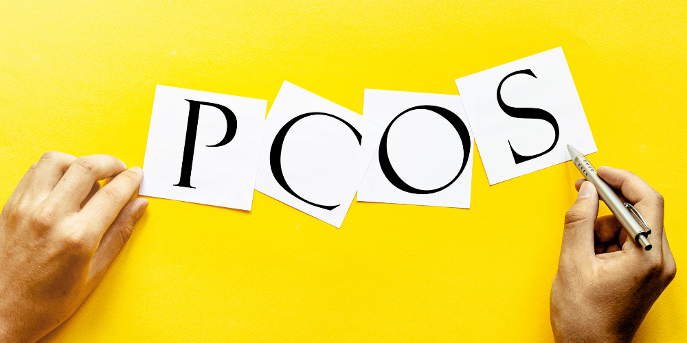 The image shows a person writing on a yellow paper with the word "PCOS" written on it. Tags include finger, person, and hand.