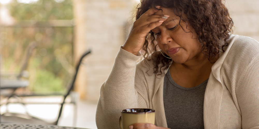 The image shows a woman sitting indoors and drinking coffee, seemingly stressed about something.