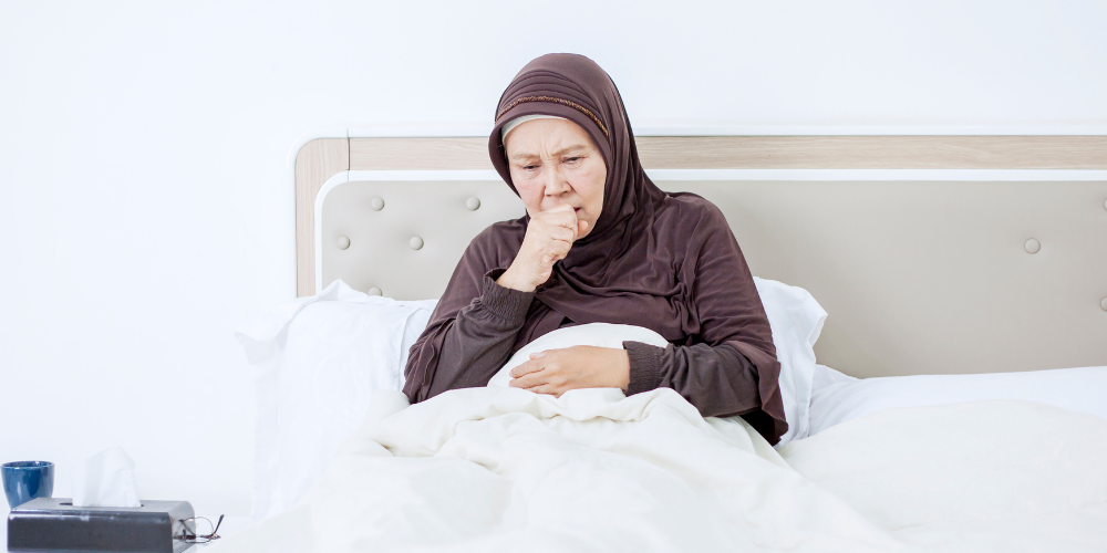 The image depicts a woman sitting on a bed in an indoor setting. The woman appears comfortable and is wearing clothing.