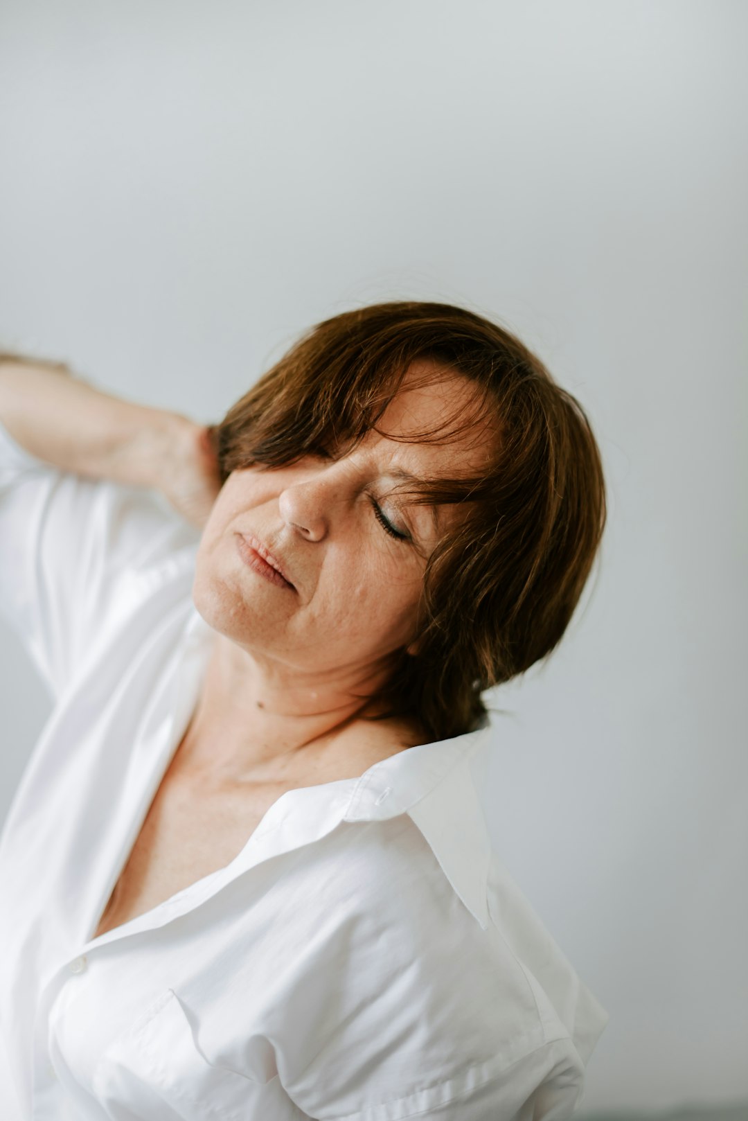 a woman in a white shirt is holding her hands behind her head