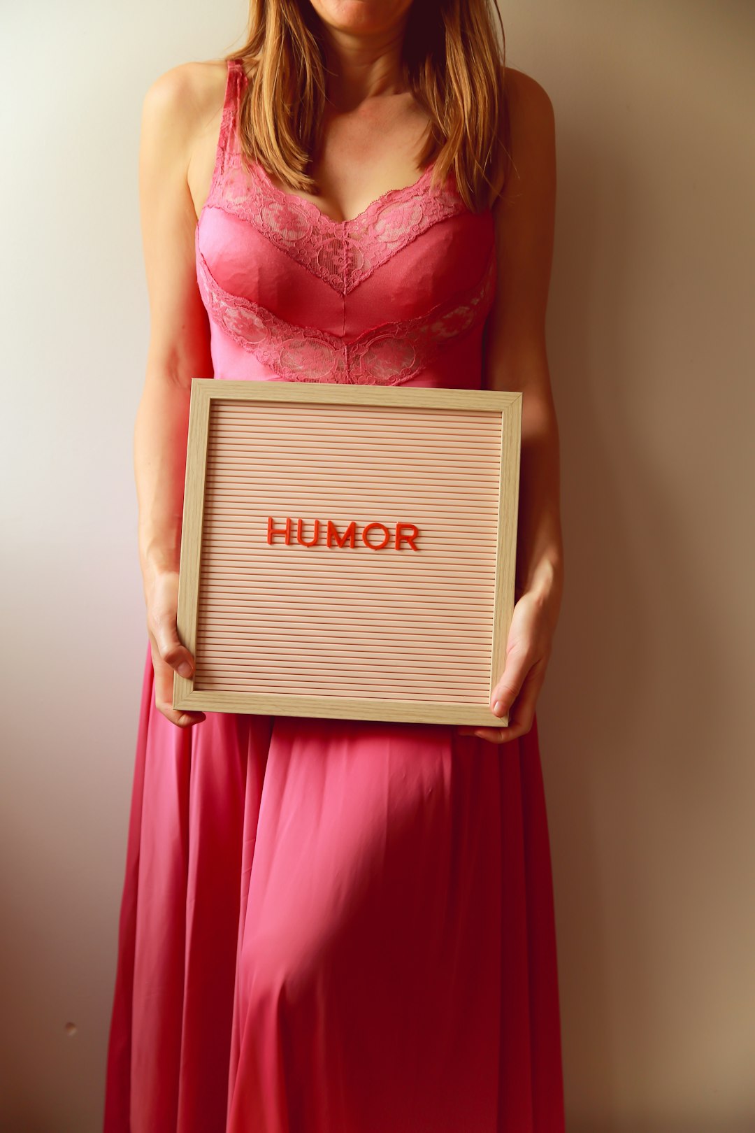 Woman in pink dress holds a board with "humor."