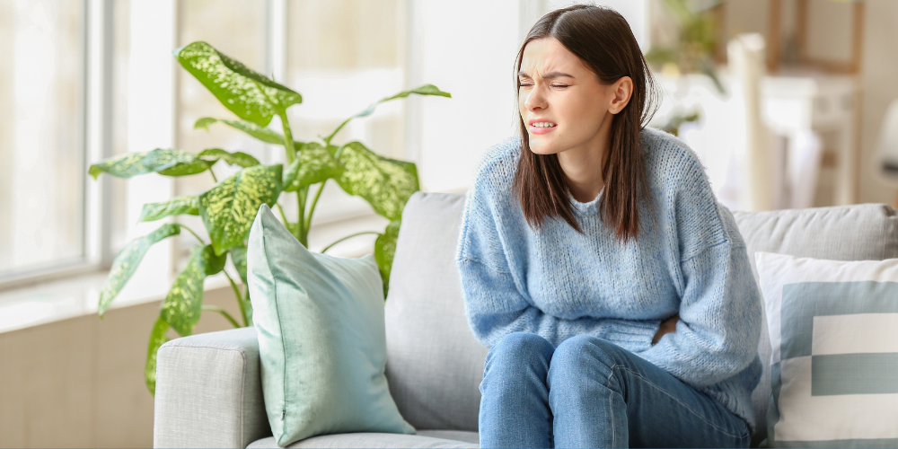 The image shows a woman sitting on a couch in a room with a houseplant by the window.