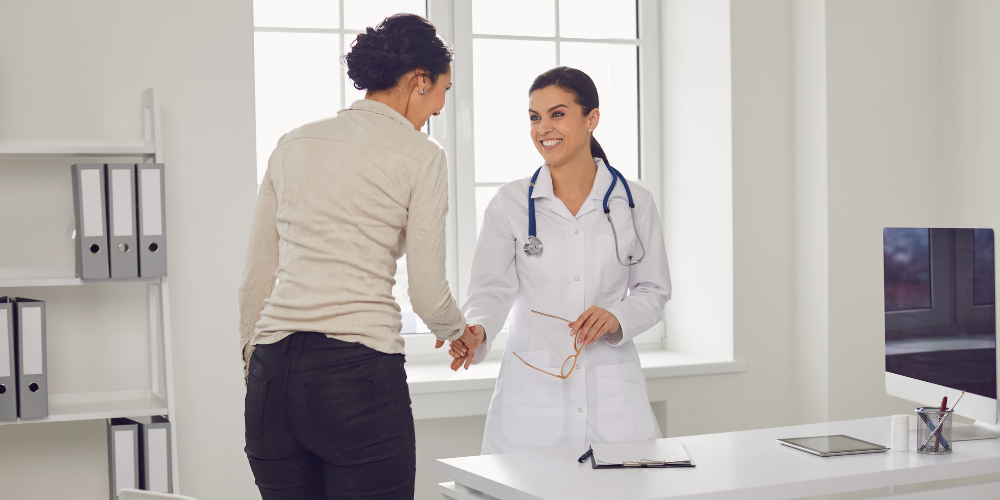 The image shows a doctor and a patient greeting each other in an office setting