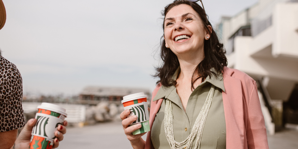 a woman smiling and having a cup of coffee outside