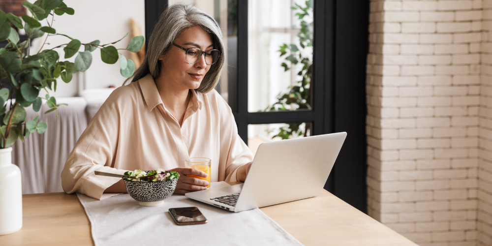 a woman looking at the laptop with a bowl of salad and a juice