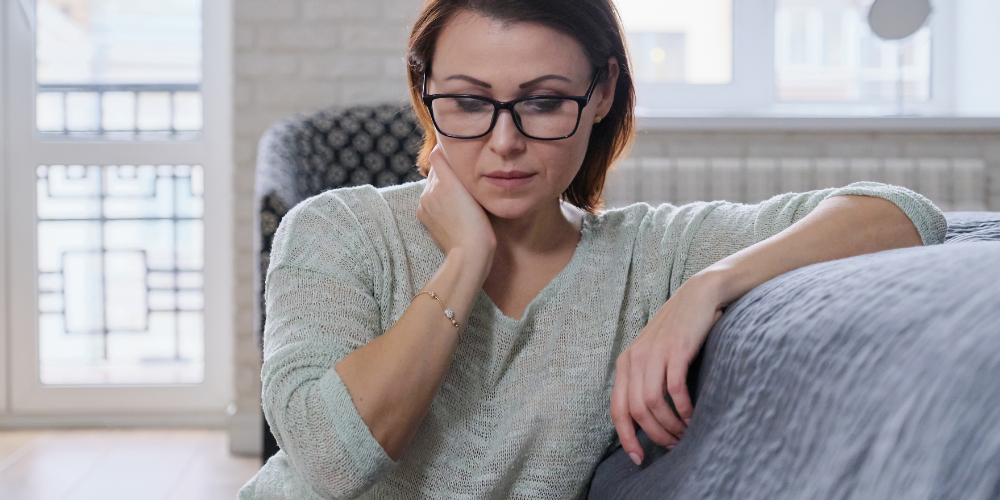 The image shows a woman indoors, wearing glasses.