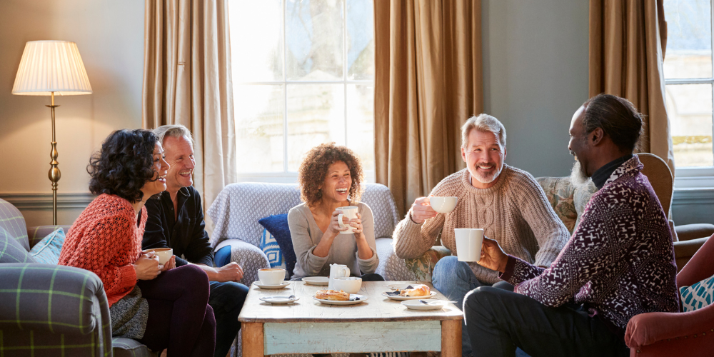 A group of people is sitting on a couch, enjoying each other's company and drinking tea.