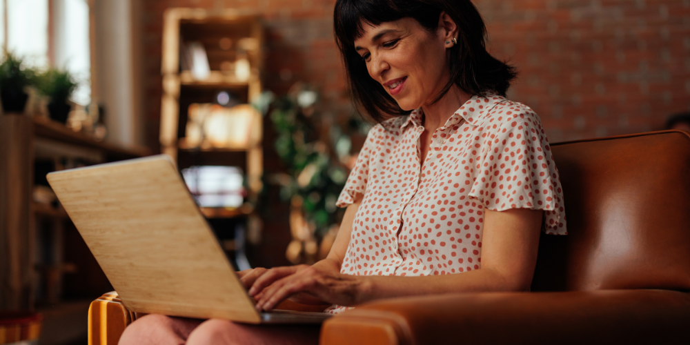 The image features a person sitting indoors, using a laptop while seated on a chair