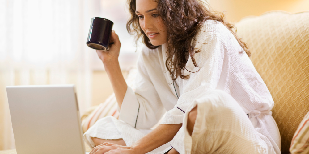 The image shows a woman looking at her laptop indoors.